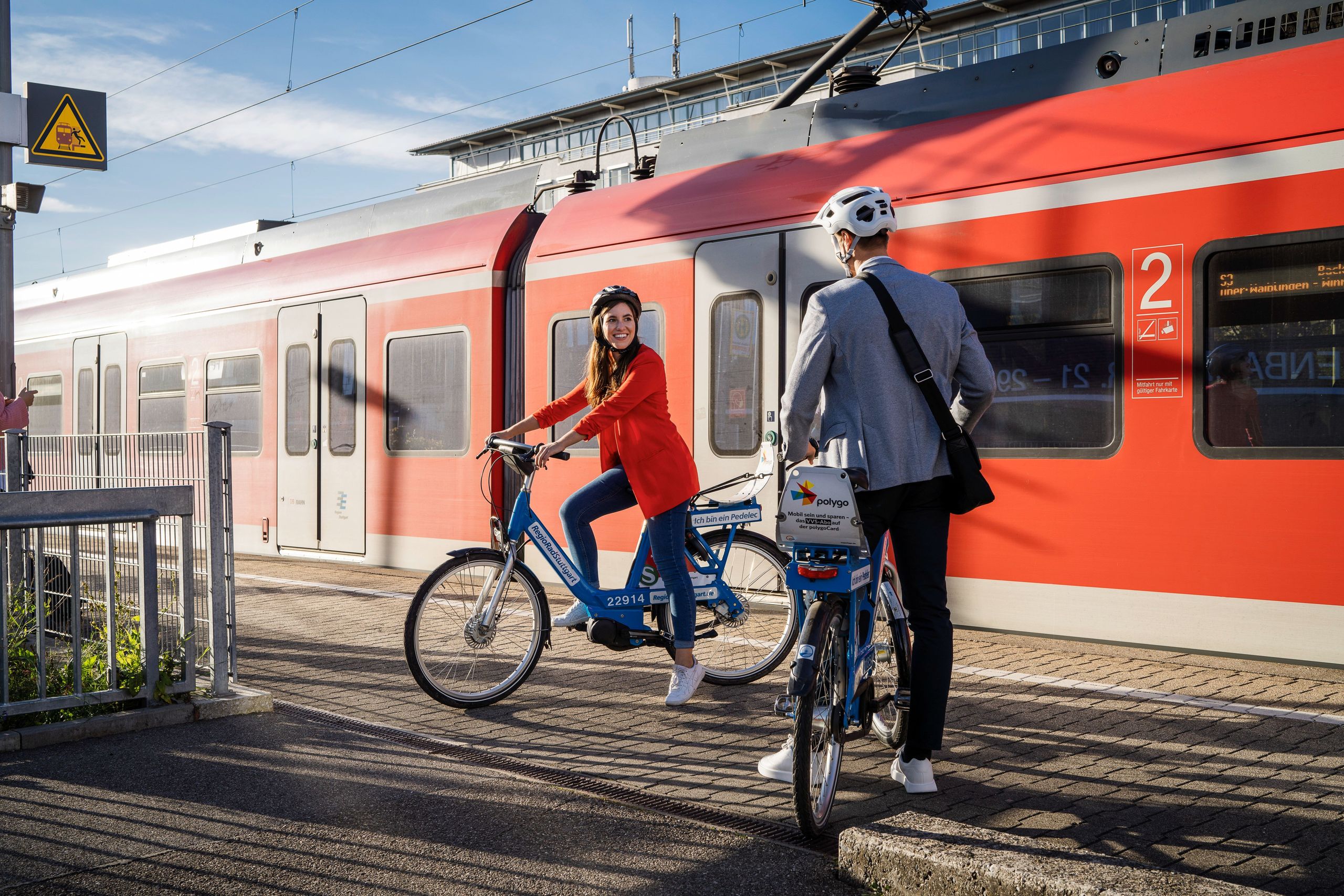 Frau und Mann stehen mit RegioRadStuttgart Pedelecs am Bahngleis vor einem Zug